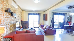 A spacious living room with a red sofa, a television, and a dining area with a chandelier. - 3 Bedroom Villa, Private Pool, 250m to Latchi Beach (Latchi)
