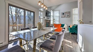 A spacious living area with a large glass table, comfortable seating, a fireplace, and a view of the outdoors. - Brand New Modern-Chic Townhome with Deck! (Tannersville)