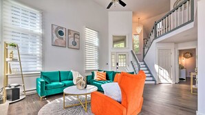 A spacious living room with a green sofa, an orange armchair, and a round coffee table. A staircase leads to an upper level. - Brand New Modern-Chic Townhome with Deck! (Tannersville)