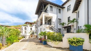 A multi-story building with a white facade, balconies, and a cobblestone pathway leading to the entrance. - This luxury home features a private pool  and stunning ocean views (Catalinas)