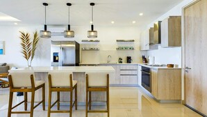A modern kitchen with a central island, bar stools, pendant lighting, and wooden cabinetry. - Condo Mirador-Breathtaking Ocean View (Tamarindo)