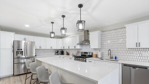 A modern kitchen with white cabinetry, a large island, stainless steel appliances, and pendant lighting. - 4 Bed Mid Century Modern w/ Pool, Putting Green, Wood Fired Pizza Oven, Sleeps 9 (Phoenix)