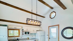 Een moderne keuken met witte kasten, een houten kookeiland met barkrukken, een hanglamp en een ronde spiegel aan de muur.