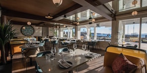 En rummelig restaurant med flere spiseborde og stole, store vinduer med udsigt til det fri, og et moderne interiør.