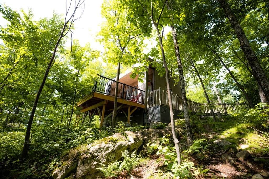 A cabin in a forest with a wooden deck and a metal railing.