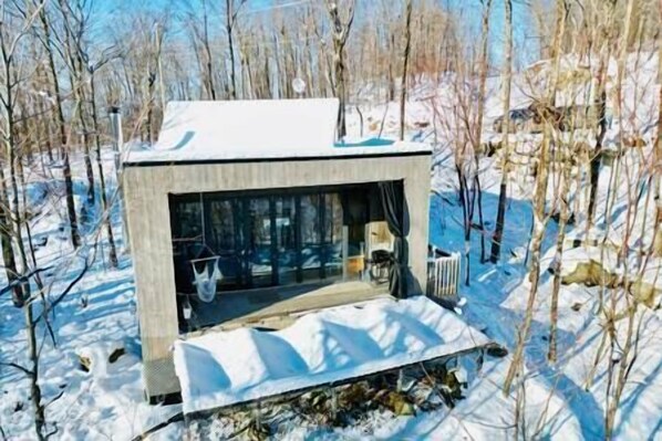 Une cabane moderne, recouverte de neige, avec une façade en verre, entourée d’une forêt.