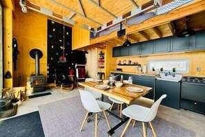 A modern kitchen with wooden cabinets, a dining table with chairs, and a fireplace. - Les Hauts Boisés, Écogite, 6pers (Eastman)