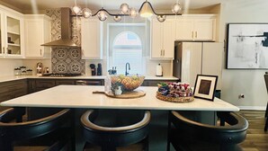 Una cocina moderna con una isla central, iluminación colgante y un ventanal grande.