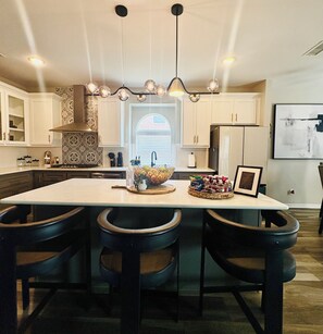 Een moderne keuken met een centraal eiland, hanglampen en een groot raam.