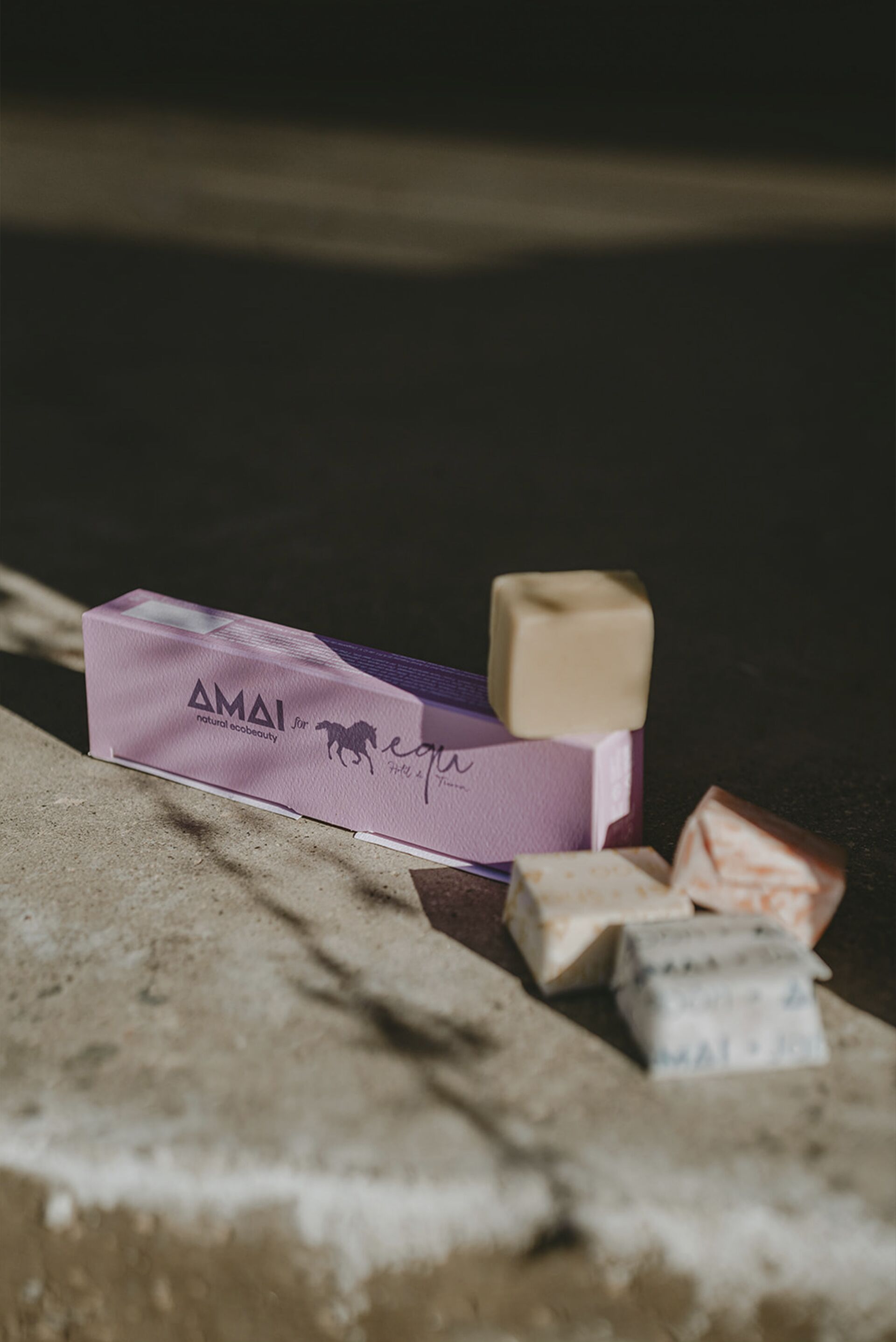Una scatola etichettata “AMAI” con un logo e del testo, insieme a diversi altri piccoli oggetti rettangolari su una superficie strutturata.