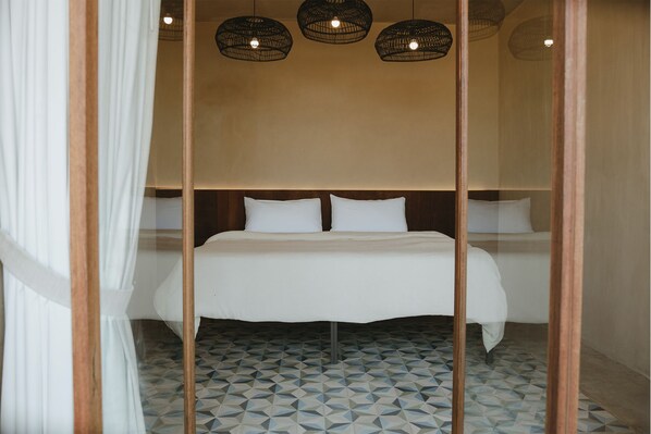 Un dormitorio con cama, ropa de cama blanca, suelo con estampado geométrico y tres lámparas colgantes.