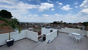 A rooftop terrace with a white table and chairs, a potted plant, and a view of the cityscape. - Amazing Apartment With Jacuzzi and City Views! (Cali)
