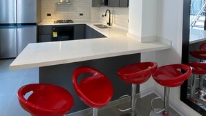A modern kitchen with a central island, stainless steel appliances, and red bar stools. - Amazing Apartment With Jacuzzi and City Views! (Cali)