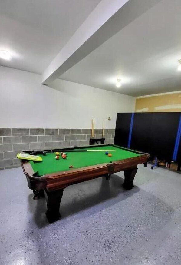 Une table de billard avec des billes et des queues, un mur de briques et un rideau bleu.