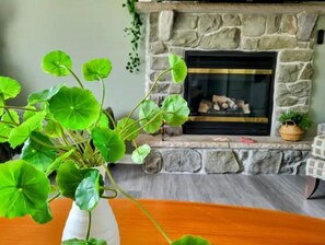 Un salon avec une cheminée en pierre, un vase blanc contenant des feuilles vertes et un panier en osier.