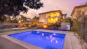 Una casa moderna de dos pisos con piscina, mobiliario exterior y un patio bien iluminado.