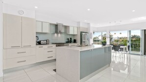 Una cocina moderna con una isla grande, muebles blancos y vistas al exterior a través de amplios ventanales.