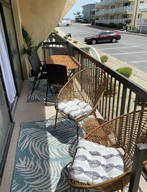 Een balkon met rieten meubilair, een kamerkleed met dessin en uitzicht op een straat met auto's en gebouwen.