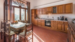 Una cocina con armarios de madera, una mesa de comedor con sillas y una ventana con cortinas.