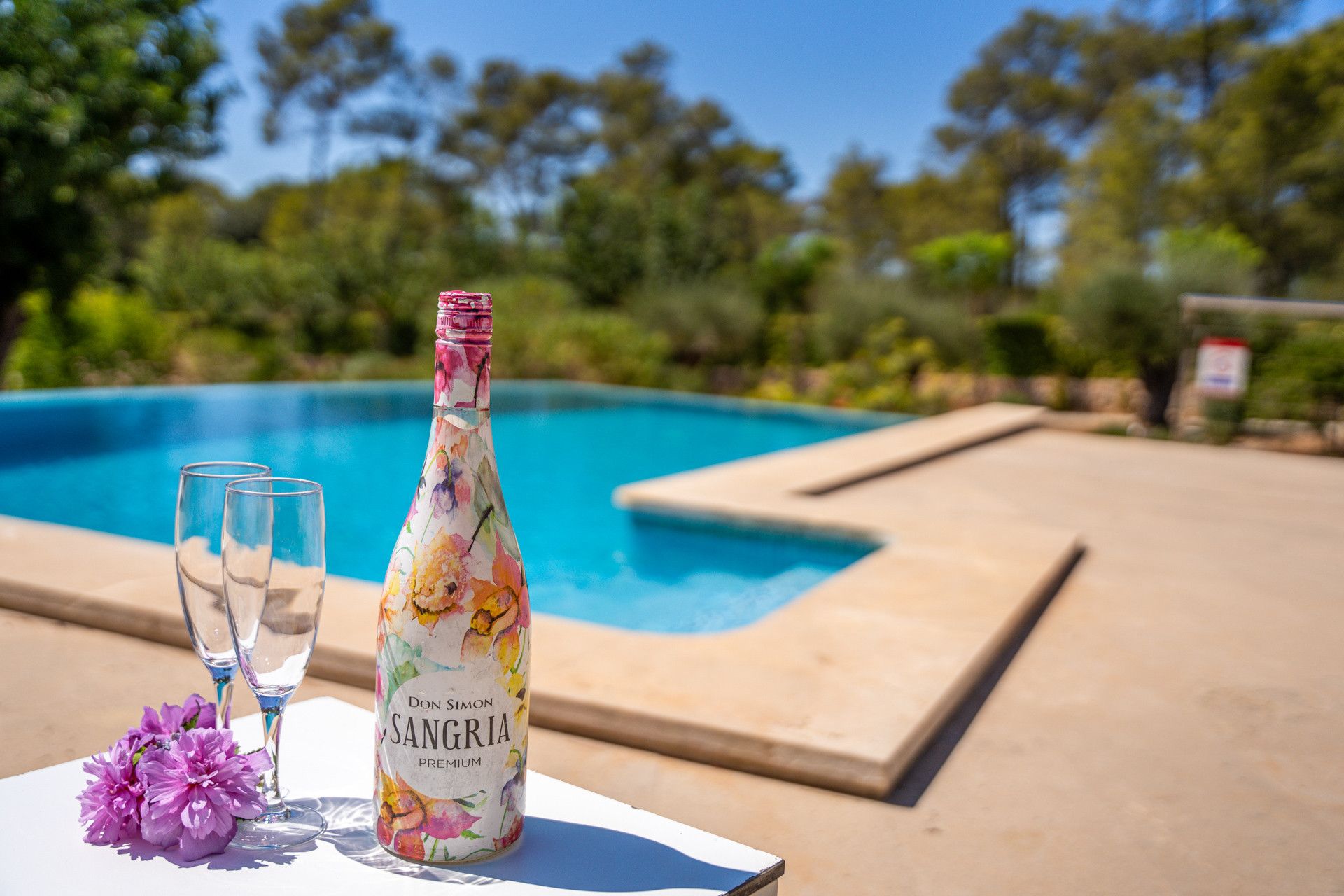 A bottle of Don Simon Sangria Premium on a table by a pool with glasses and flowers.