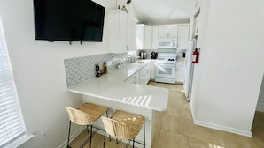 A modern kitchen with white cabinets, a central island with bar stools, a flat-screen TV mounted above the island, and a microwave above the oven. - Fun shore bungalow that is walkable to the beach!  (Lavallette)
