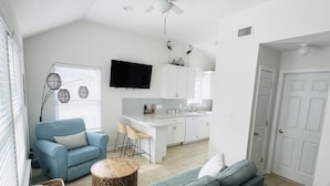 A modern living room with a blue sofa, a grey sofa, a wooden side table, and a kitchen area with white cabinets and a flat-screen TV. - Fun shore bungalow that is walkable to the beach!  (Lavallette)