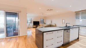 A modern kitchen with a central island, a dining area with a sofa, and a TV in the background.