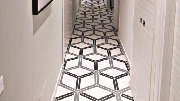 Un pasillo con piso de diseño geométrico, paredes blancas y cuadros enmarcados.