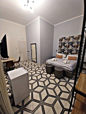 Un dormitorio moderno con piso de estampado geométrico, una cama con ropa de cama a rayas, un escritorio con una silla y un televisor montado en la pared.