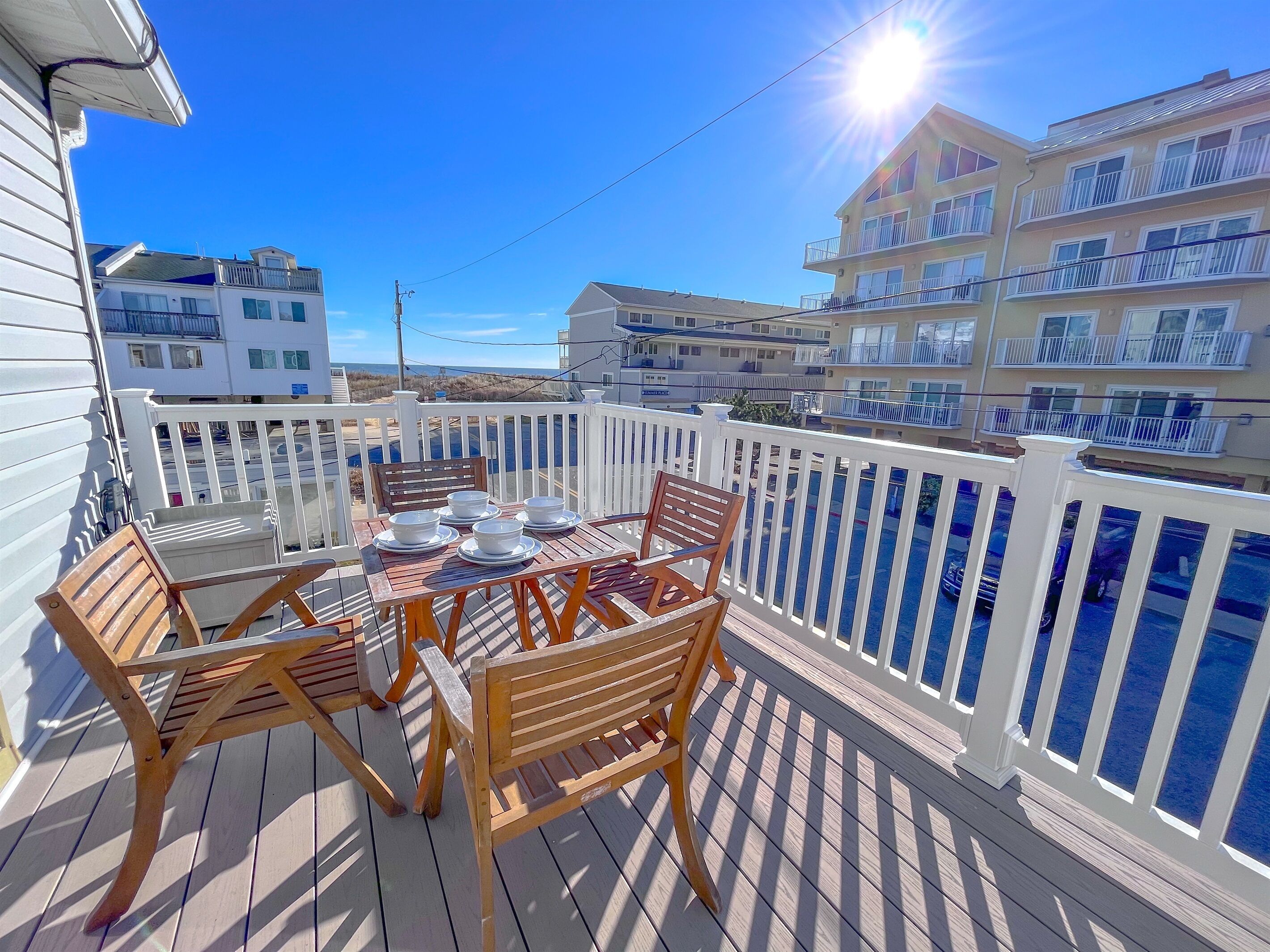 A wooden deck with a table set for dining, surrounded by white railings and overlooking a body of water.