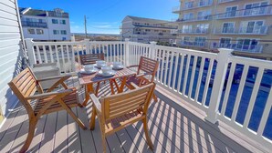 A wooden deck with a table set for dining, surrounded by white railings and overlooking a body of water.