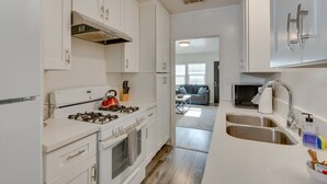 Cocina moderna con armarios blancos, estufa a gas, pileta de acero inoxidable y vista al área de estar.
