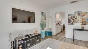 Una sala moderna con un televisor de pantalla plana, una mesa consola con objetos decorativos, un jarrón grande y arte abstracto en la pared.