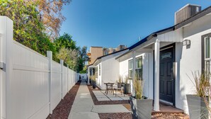 Un estrecho sendero que conduce a un edificio de fachada blanca, con una puerta negra y un pequeño patio con mesa y sillas.