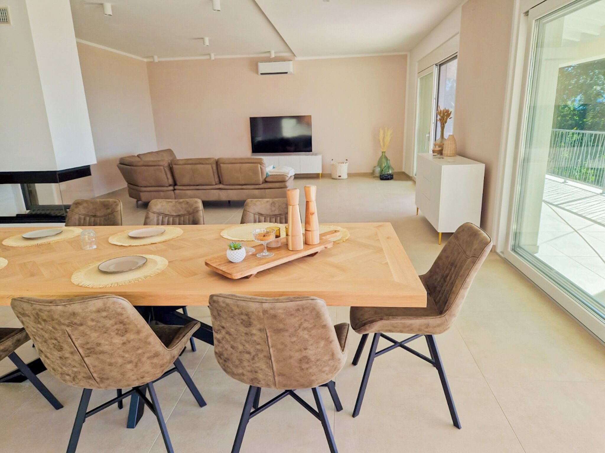 A modern dining area with a wooden table set for four, surrounded by upholstered chairs. A flat-screen TV is mounted on the wall above the seating area.