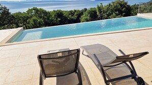 Ein Pool mit Blick auf das Meer und die Berge. Zwei Liegestühle sind vorhanden.