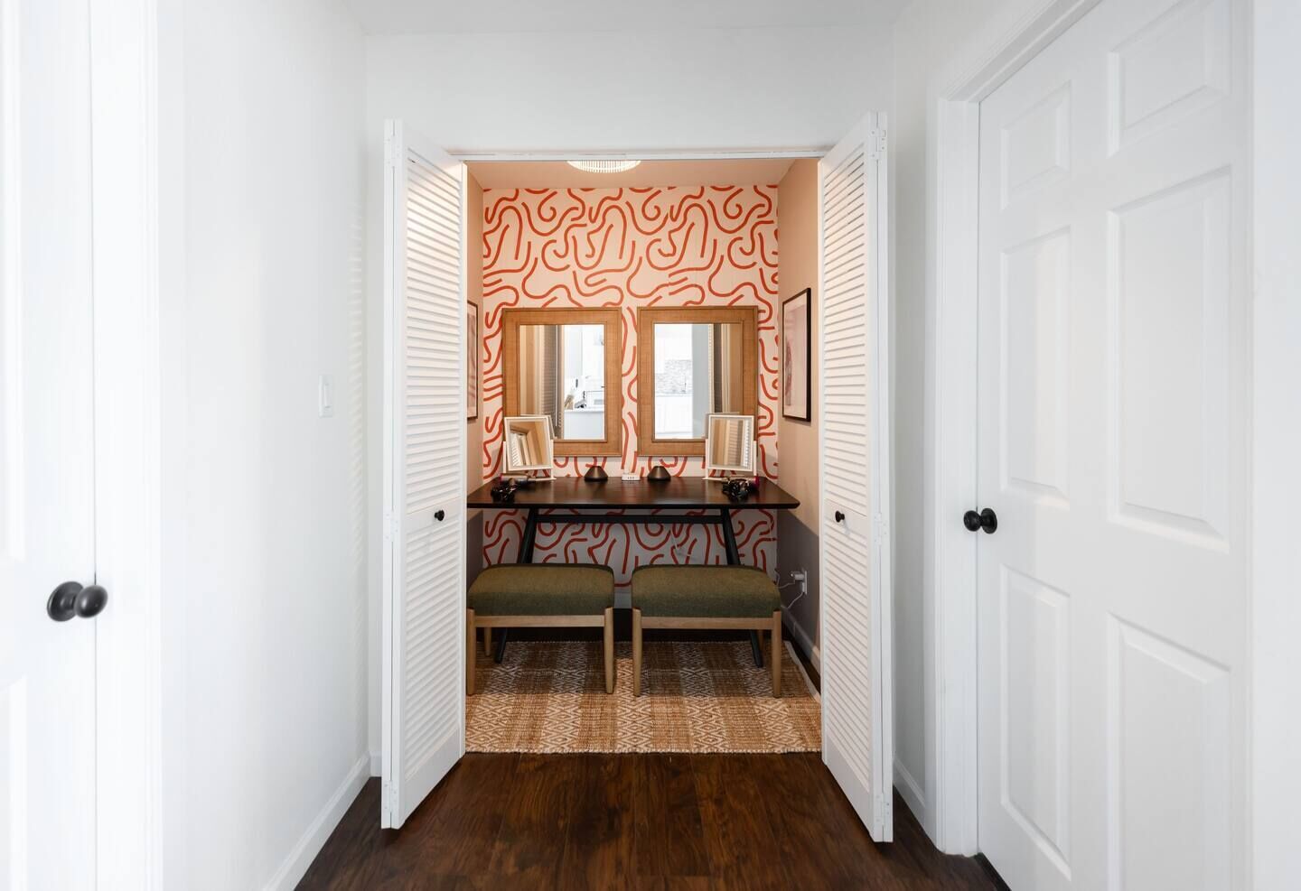 A hallway with a wooden desk, two chairs, a bench, and a patterned wall.