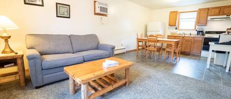 A compact living space with a sofa, coffee table, dining table, and kitchen area.