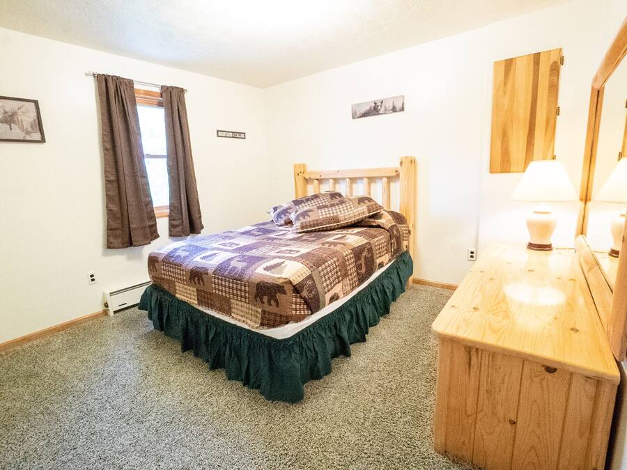 A bedroom with a wooden headboard, a bed with a patterned bedspread, a bedside table with a lamp, and a mirror.