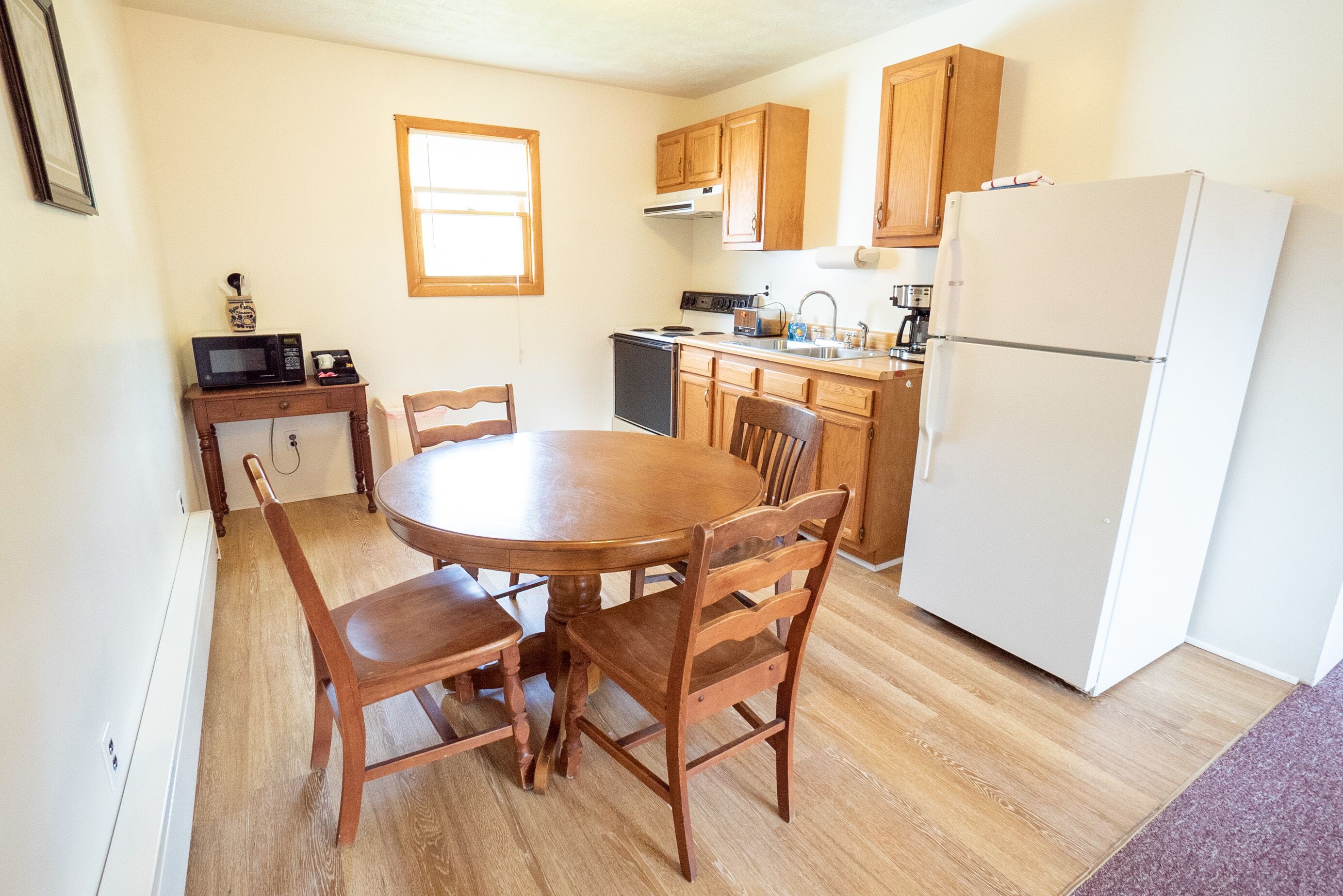 Une cuisine compacte avec des meubles en bois, un réfrigérateur blanc, un four à micro-ondes et une table à manger avec des chaises.