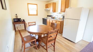 Una cocina compacta con armarios de madera, un refrigerador blanco, un microondas y una mesa de comedor con sillas.
