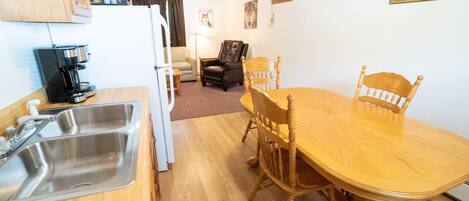 A compact kitchen with a coffee maker, a sink, and a dining area with a wooden table and chairs.