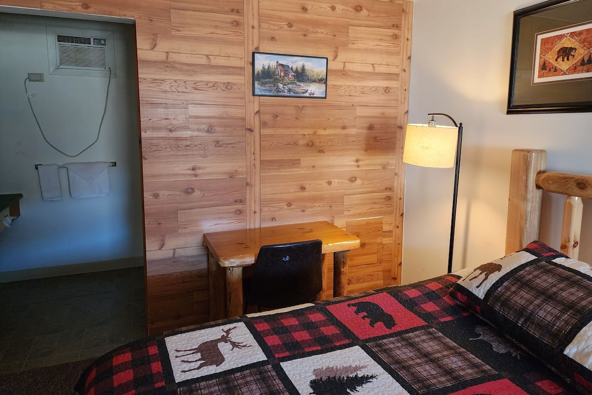 A cozy room with a wooden wall, a bed with a quilt, a desk, and a chair.