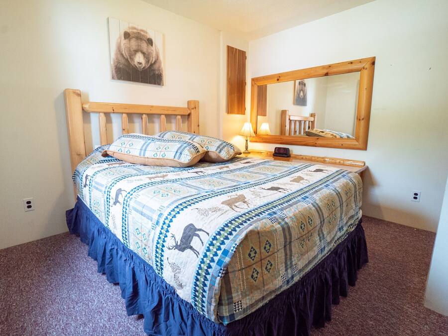Quarto com cama, cabeceira de madeira, espelho e decoração de parede com tema de urso.