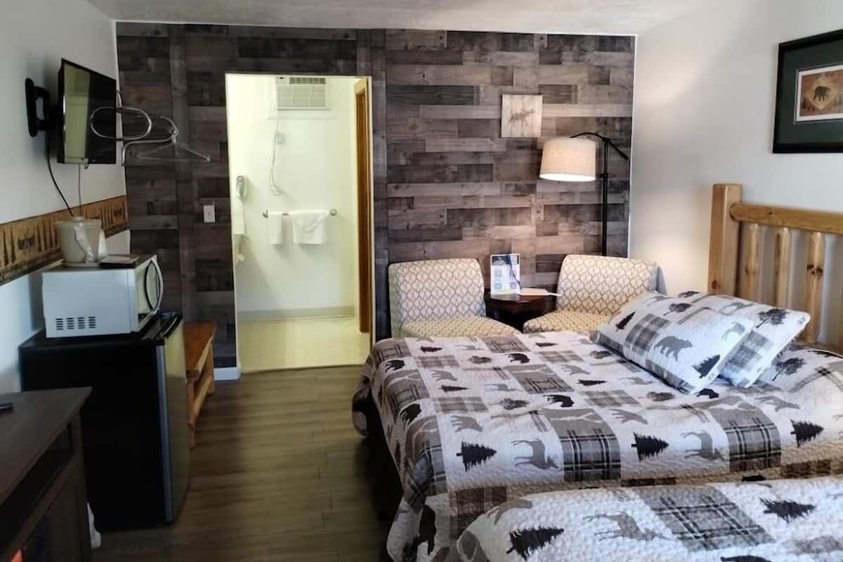 A bedroom with a bed, two chairs, a bedside table, a lamp, a microwave, and a wooden wall panel.
