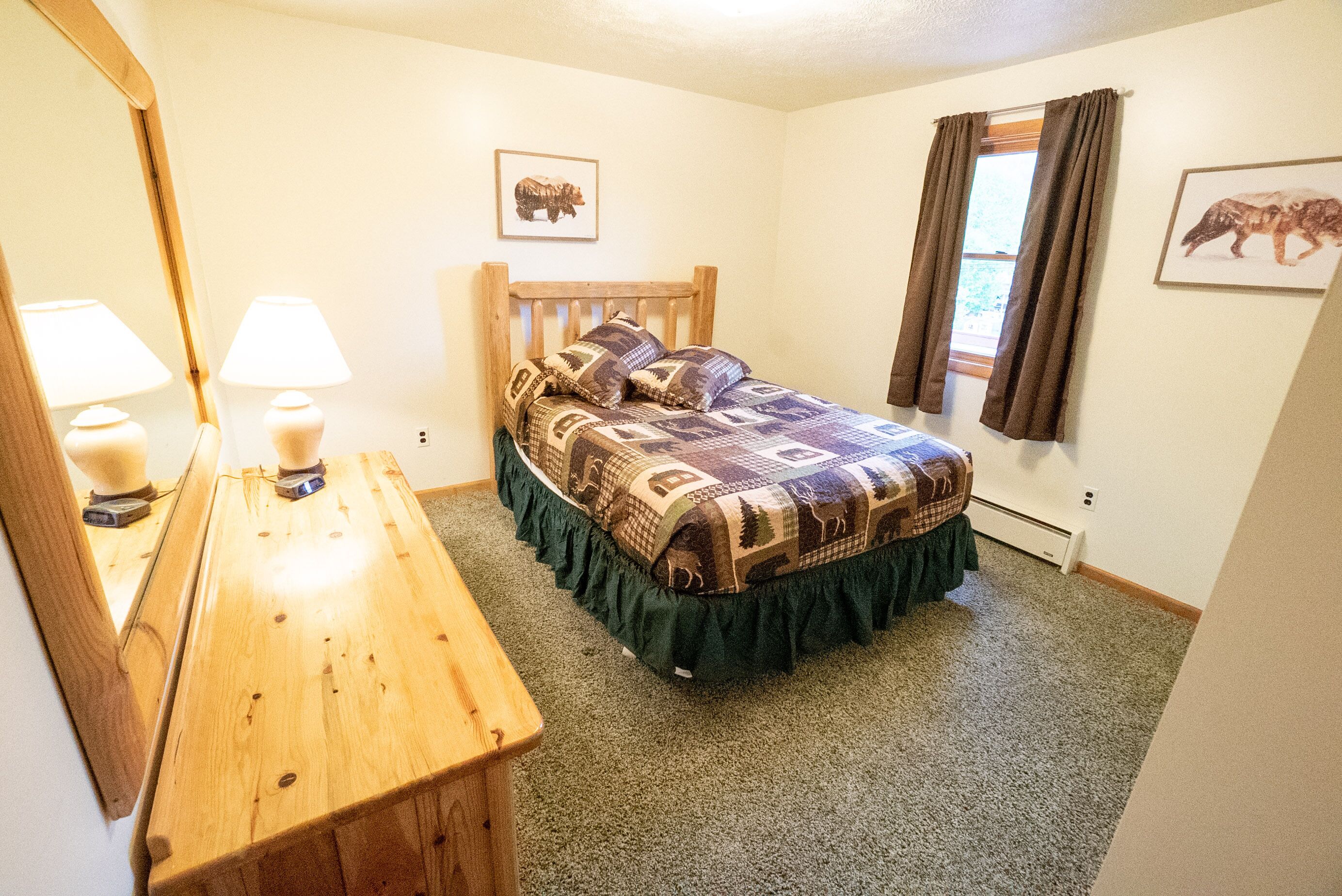 A bedroom with a wooden bed, a dresser, a mirror, and two wall-mounted lamps.
