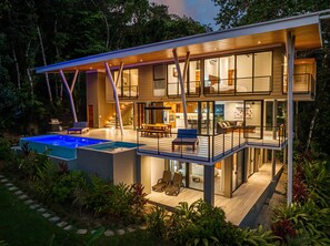 Ein modernes, zweistöckiges Haus mit Schwimmbad, Außenbereich mit Sitzgelegenheiten und gut beleuchtetem Innenraum.