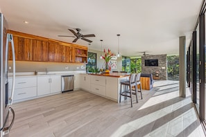 A modern kitchen with wooden cabinets, a central island, and a dining area with a sofa and chairs. - Tropical 4 Bedroom Luxury Home with Pool & Hot Tub (Savegre)