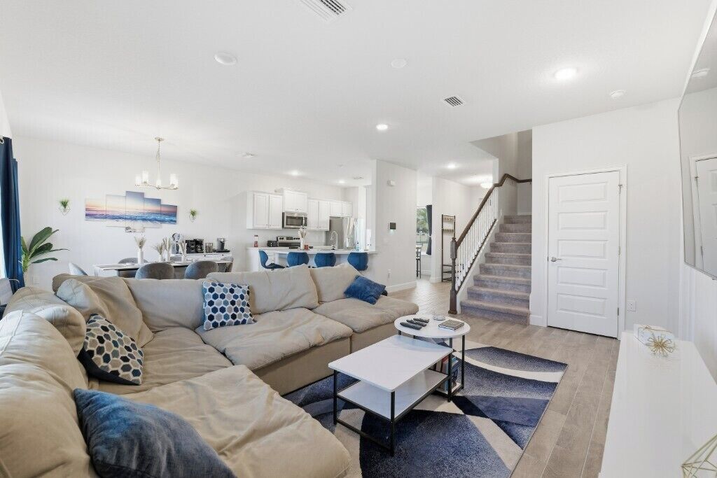 Ein modernes Wohnzimmer mit einem beigefarbenen Ecksofa, einem Couchtisch und einer Treppe, die zu einer oberen Etage führt.