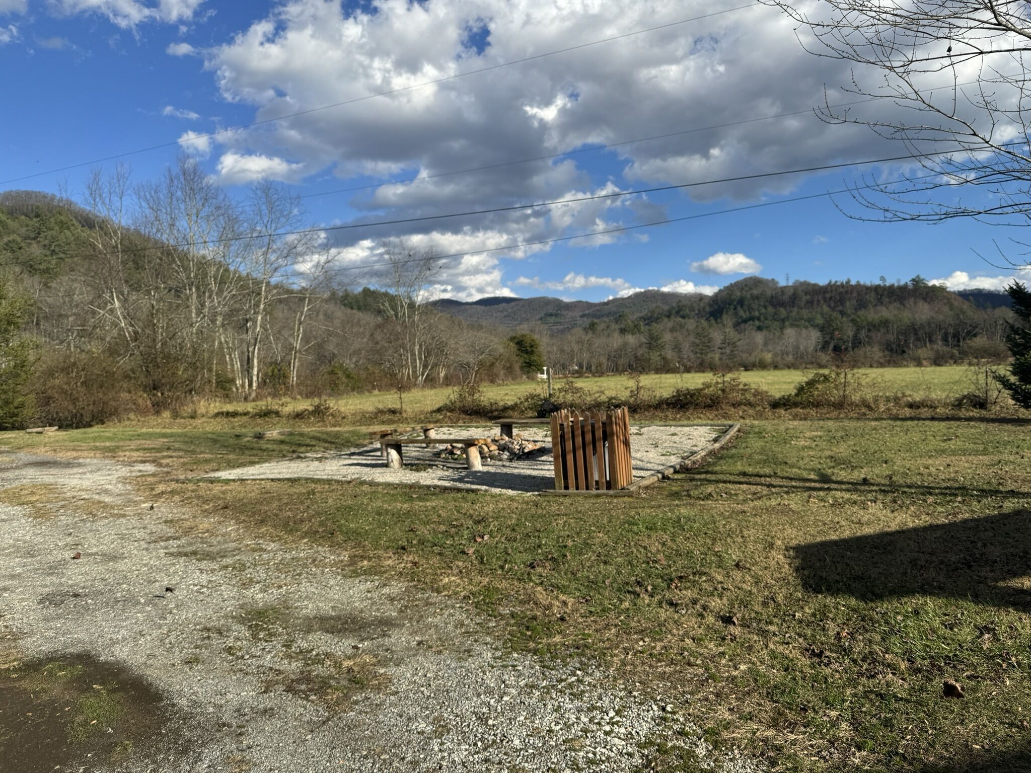 Un’area di parcheggio sterrata con un tavolo da picnic e una struttura in legno, immersa in prati verdi e alberi.
